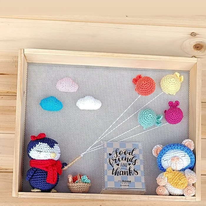 Cuadro de decoración infantil Brisa con figuras amigurumi, globos en tonos pastel y marco de madera natural para habitación de bebé.