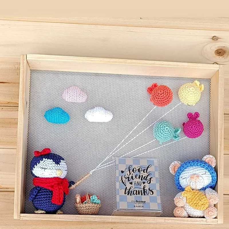 Cuadro de decoración infantil Brisa con figuras amigurumi, globos en tonos pastel y marco de madera natural para habitación de bebé.
