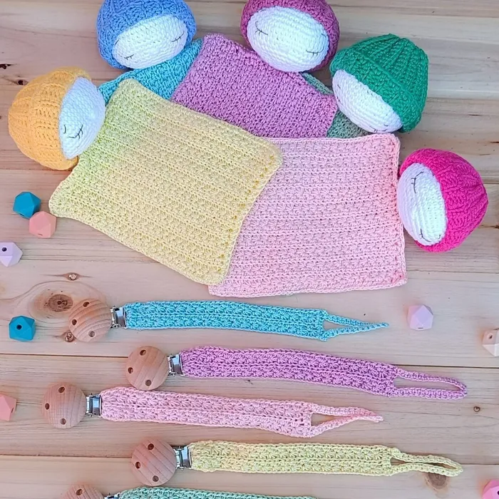 Set en crochet para bebé modelo Origen con dudú de la calma y chupetero coordinados en tonos pastel sobre fondo neutro.